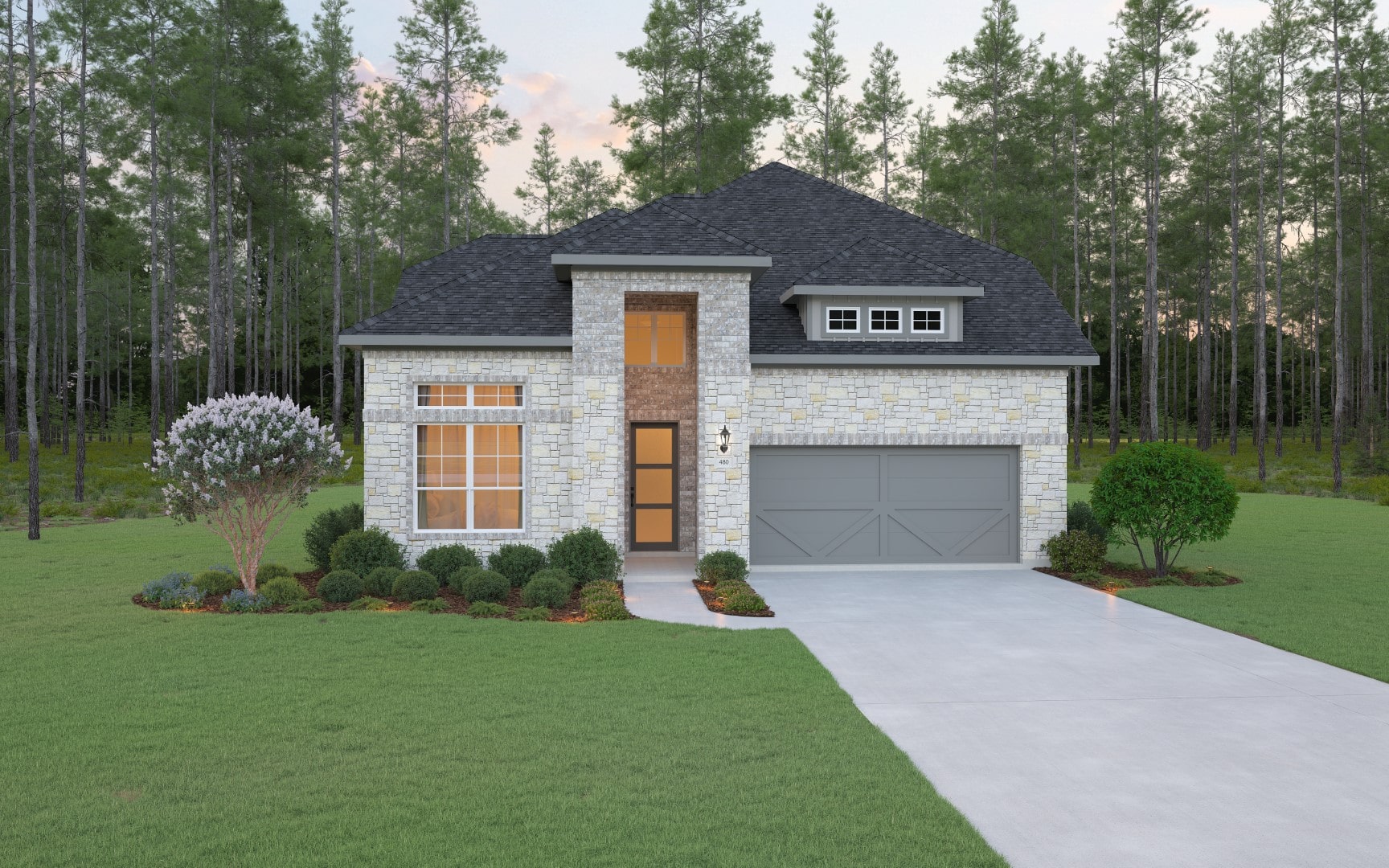 A modern stone house with a dark gray roof, two-car garage, and large windows, surrounded by green grass, shrubs, and trees, set against a dense forest backdrop at sunset.
